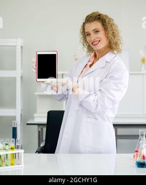 Jeune scientifique blond tenant un ordinateur de tablette à écran vide. Atmosphère de travail en laboratoire chimique. Banque D'Images
