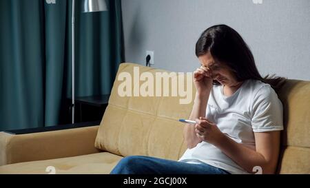 La jeune femme avec la frustration regarde le test de grossesse Banque D'Images