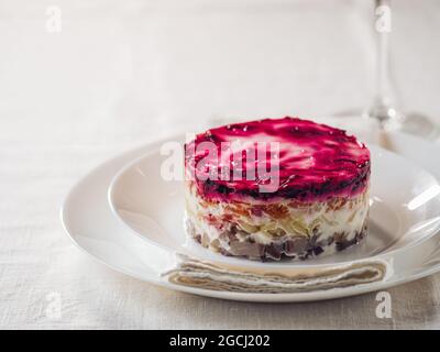 Salade de hareng superposée sous un manteau de fourrure sur la table. Portion de salade russe traditionnelle avec hareng, betterave et autres légumes sur nappe blanche. Copier l'espace Banque D'Images