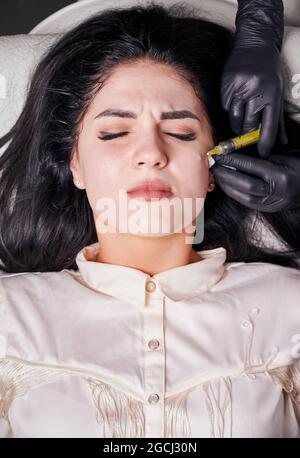 Gros plan vertical de l'injection de la procédure de plasmoliftation. Injection de plasma dans la peau sur les pommettes du patient. Traitement au plasma riche en plaquettes. Vue de dessus. Concept de soins de beauté et de soin de la peau. Banque D'Images