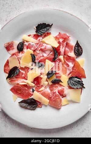 Fond alimentaire prosciutto coppa di parme tranches de jambon avec parmesan et basilic foncé sur plaque claire sur fond texturé. Vue de dessus, orientation verticale Banque D'Images