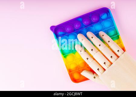 Pop-it jouet et main artificielle sur fond rose. Le robot clique sur pop it. Concept anti-stress. Copier l'espace. Vue de dessus Banque D'Images