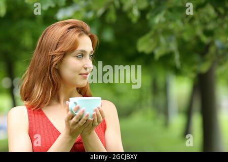 Femme sérieuse tenant une tasse de café contemplant la vue dans un parc Banque D'Images