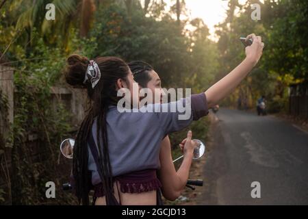 Couple en vélo traversant le village de Goa, en Inde. Prise de selfie sur un téléphone portable Banque D'Images