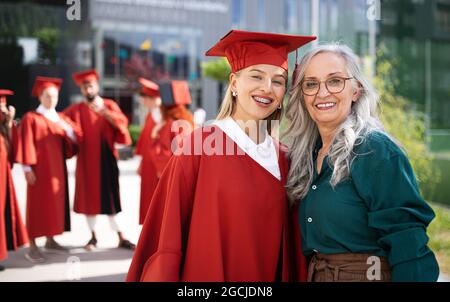 Portrait d'un étudiant universitaire joyeux avec une mère regardant l'appareil photo à l'extérieur, concept de remise des diplômes. Banque D'Images