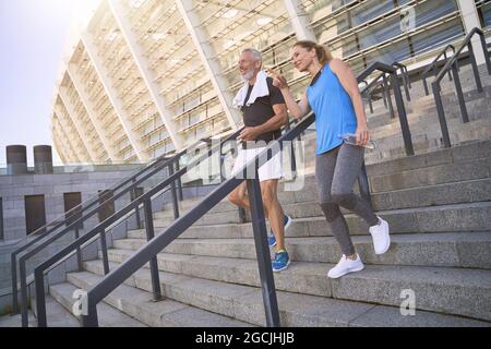 Couple d'âge moyen, homme et femme dans les vêtements de sport marchant dans les escaliers après s'exercer ensemble à l'extérieur Banque D'Images