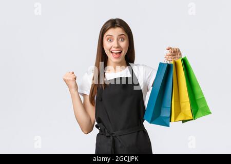 L'employé du magasin est dans une pompe à tablier noir et se réjouit, souriant heureux de tenir la commande du client, de remettre des sacs avec les articles achetés Banque D'Images