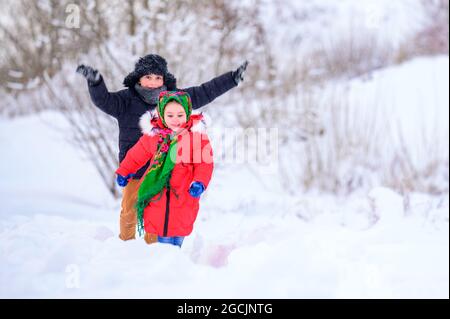 Frère et sœur marchent dans une cour enneigée, s'amusant avec de la neige. Nouveau Banque D'Images