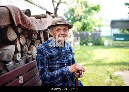 Portrait d'un homme âgé assis sur un banc à l'extérieur dans le jardin, se reposant et regardant la caméra. Banque D'Images