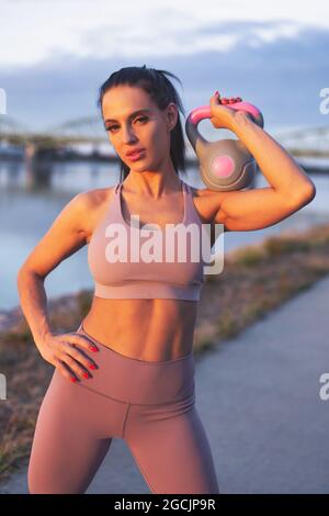 Jeune femme caucasienne tenant la kettlebell sur l'épaule au bord de la rivière Banque D'Images