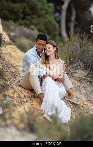 Contenu multiracial couple de jeunes mariés assis dans les bois et embrassant le jour du mariage Banque D'Images