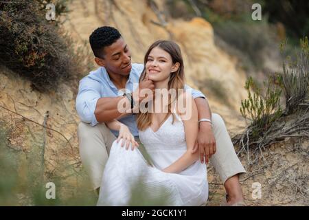 Contenu multiracial couple de jeunes mariés assis dans les bois et embrassant le jour du mariage Banque D'Images