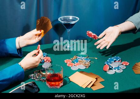 Rognez des amis féminins méconnaissables assis à la table verte avec des cartes et des jetons de poker tout en jouant Banque D'Images