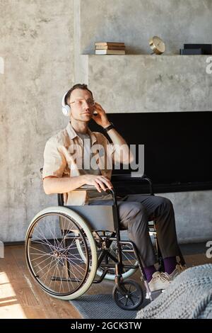 Portrait vertical complet d'un adulte handicapé en fauteuil roulant écoutant de la musique à la maison Banque D'Images