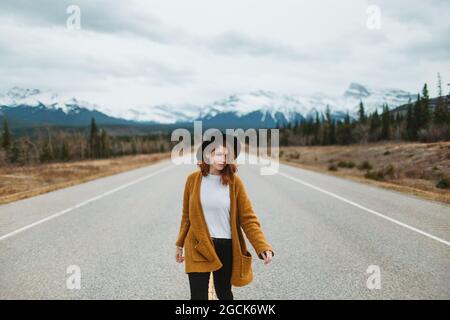 Femme touriste en vêtements décontractés marchant sur la route David Thompson contre les montagnes enneigées de l'Alberta, Canada Banque D'Images