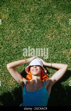 Vue de dessus d'une jeune femme joyeuse à tête rouge, couché sur l'herbe par une belle journée d'été Banque D'Images