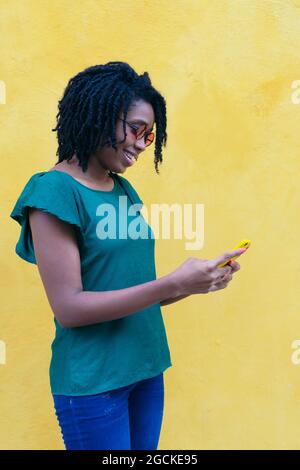 Portrait d'une jeune femme africaine envoyant un SMS avec un smartphone dans la rue. Banque D'Images