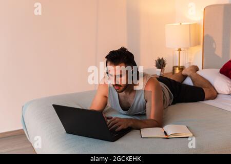 Homme concentré dans un casque couché sur le lit et en tapant sur un netbook à la maison Banque D'Images