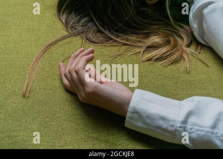 Haut angle de la récolte anonyme femme avec des cheveux justes vêtu d'une chemise blanche avec des manches longues couché sur le tissu vert Banque D'Images