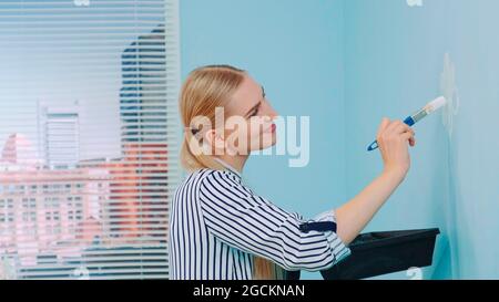 Gros plan de fille en train de peindre des fleurs sur le mur bleu dans un bureau moderne. Banque D'Images