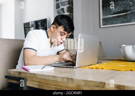 Focus latin adolescent garçon avec le syndrome de Down navigation netbook tout en étant assis à la table et étudiant en ligne de la maison Banque D'Images