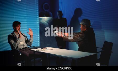 Le délinquant multiracial saisit l'arme et menace de nuire aux détectives pendant le processus d'interrogatoire. Ils ont très peur et se lèvent les mains. Banque D'Images