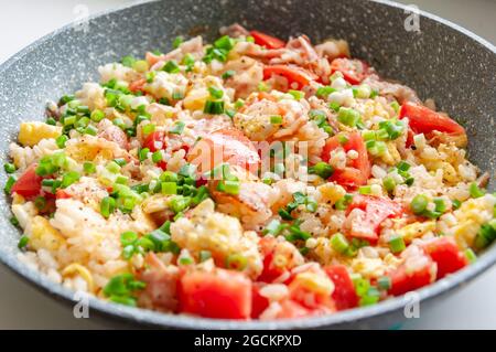 Remuez le riz frit dans la poêle. Riz savoureux cuit avec des légumes et du bacon dans une casserole sur la table. Banque D'Images