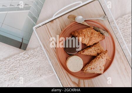 Vue de dessus des biscuits sandwich et croissant servis sur l'assiette avec du pain de grain sur le plateau pour le petit déjeuner au lit Banque D'Images