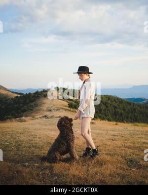 Vue latérale de la femme propriétaire avec un chien obéissant de Labradoodle debout dans les montagnes Banque D'Images