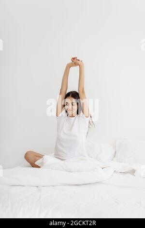 Jolie jeune femme se réveillant au lit et étirant ses bras. Banque D'Images