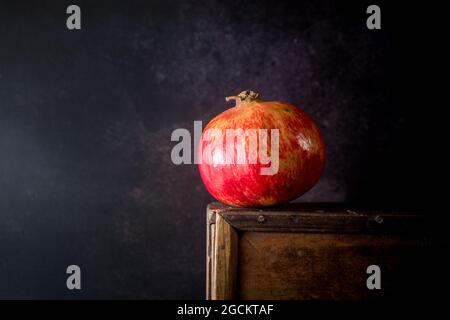 Composition à vie fixe avec des fruits de grenade entiers rouge vif placés sur un support en bois sur fond noir Banque D'Images