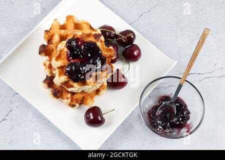 Gros plan de gaufres sur une assiette blanche avec confiture de cerises. Banque D'Images