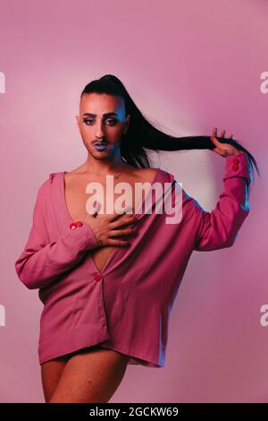 Portrait de femme barbu transgenre glamour dans un maquillage sophistiqué posé sur fond rose au studio regardant l'appareil photo Banque D'Images