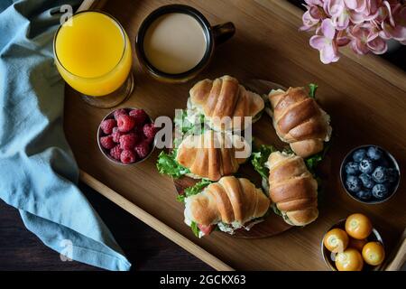 Délicieux croissants avec légumes servis sur plateau avec cappuccino et jus d'orange préparés pour le petit déjeuner français et placés sur du tabl en bois Banque D'Images