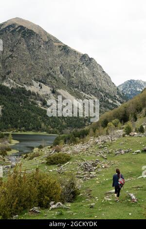 Vue arrière d'une randonneur anonyme marchant le long d'une pente verte dans la vallée de la chaîne de montagnes des Pyrénées Banque D'Images