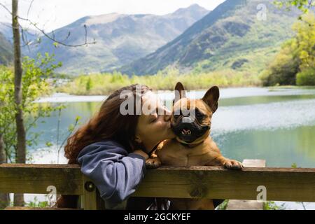 Charmante femme voyageant embrassant mignon Bulldog français près de l'étang dans la chaîne de montagnes des Pyrénées Banque D'Images