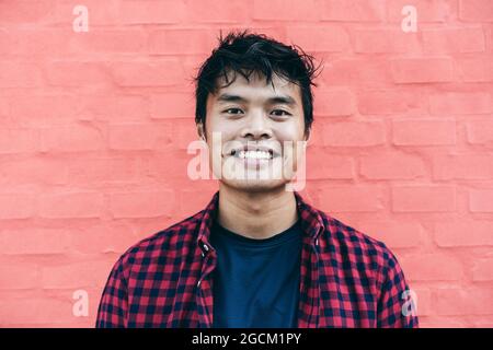 Portrait d'un homme asiatique heureux : un jeune homme asiatique confiant se fait un plaisir de sourire tout en se posant devant l'appareil photo sur un fond rouge Banque D'Images