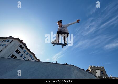 De dessous de jeune homme courageux skieur saut avec le skateboard et exécution de cascades dans le parc de skate le jour ensoleillé contre le ciel bleu Banque D'Images