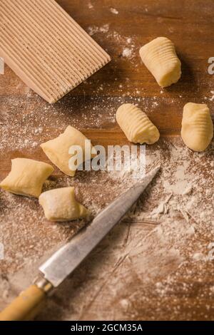 Vue de dessus des morceaux de pâte molle crue placés sur une table en bois recouverte de farine près du bord-côtes et du couteau pendant la préparation des gnocchi dans la cuisine Banque D'Images