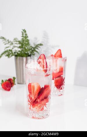 Boisson rafraîchissante d'été avec des fraises fraîches en tranches et des glaçons avec de l'eau servis dans des verres sur une table blanche Banque D'Images