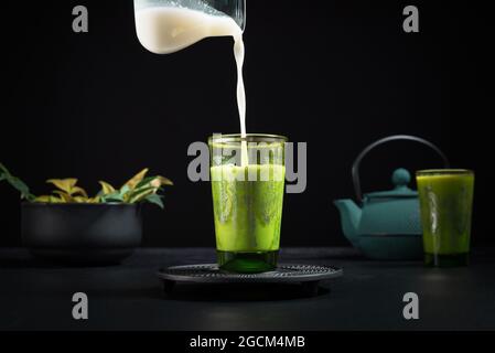 Le lait frais est versé du pot dans une tasse en verre avec du thé matcha placé sur la table avec la théière et la vaisselle pendant la cérémonie traditionnelle Banque D'Images