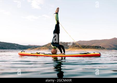 Vue latérale d'un surfeur pratiquant le yoga sur la tête de lit posé sur le panneau SUP en mer au coucher du soleil Banque D'Images