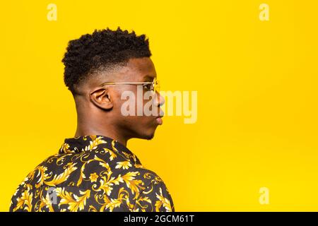 Portrait d'un homme afro-américain peu émotionnel dans une tenue tendance, debout sur fond jaune dans un studio qui regarde loin Banque D'Images