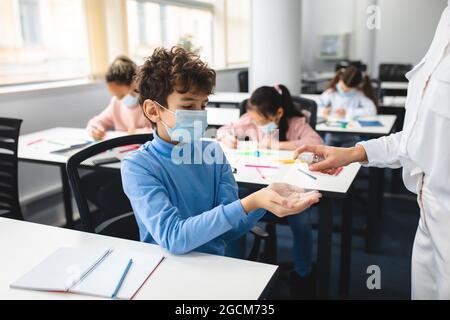 Enseignant appliquant un assainisseur antibactérien sur les mains de l'élève Banque D'Images