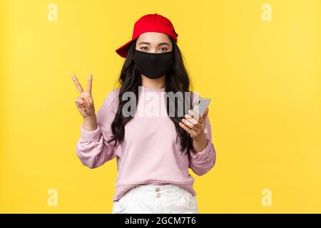 Covid-19, style de vie social-distancing, concept de prévention de la propagation du virus. Jeune fille asiatique adorable dans un masque protecteur et un capuchon rouge, rencontre des amis Banque D'Images