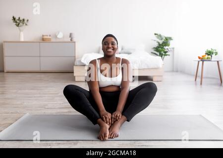 Femme noire gaie et de taille plus faisant du yoga sur tapis de sport à la maison, espace libre Banque D'Images