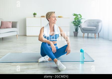 Femme sportive souriante prenant une pause en faisant de l'exercice à la maison Banque D'Images