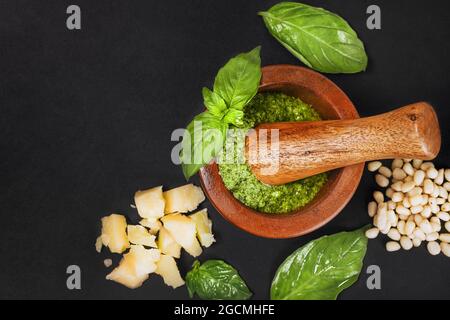 Ingrédients de la recette sauce italienne pesto. Sauce pesto verte maison avec basilic, pignons, ail, citron, huile d'olive et mortier de bois sur fond noir foncé Banque D'Images