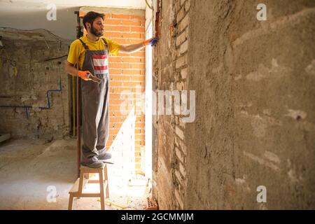 Jeune bâtisseur briser un mur de maison avec un marteau et un burin. Banque D'Images