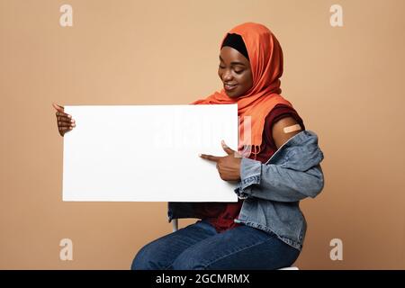 Une femme musulmane noire positive s'est vaccinée, pointant sur un écriteau vierge Banque D'Images